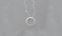 Buy handmade geometric jewellery by Elin Horgan at The Biscuit Factory. Image shows a fine silver chain with a double circle pendant attached sat on a grey background.