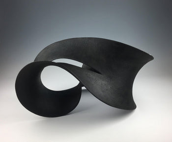 View and buy sculpture by Adrian Bates at The Biscuit Factory, a Newcastle art gallery. Image shows a black ceramic sculpture which curves like thick ribbon doubling back on itself to create something resembling an infinity symbol.