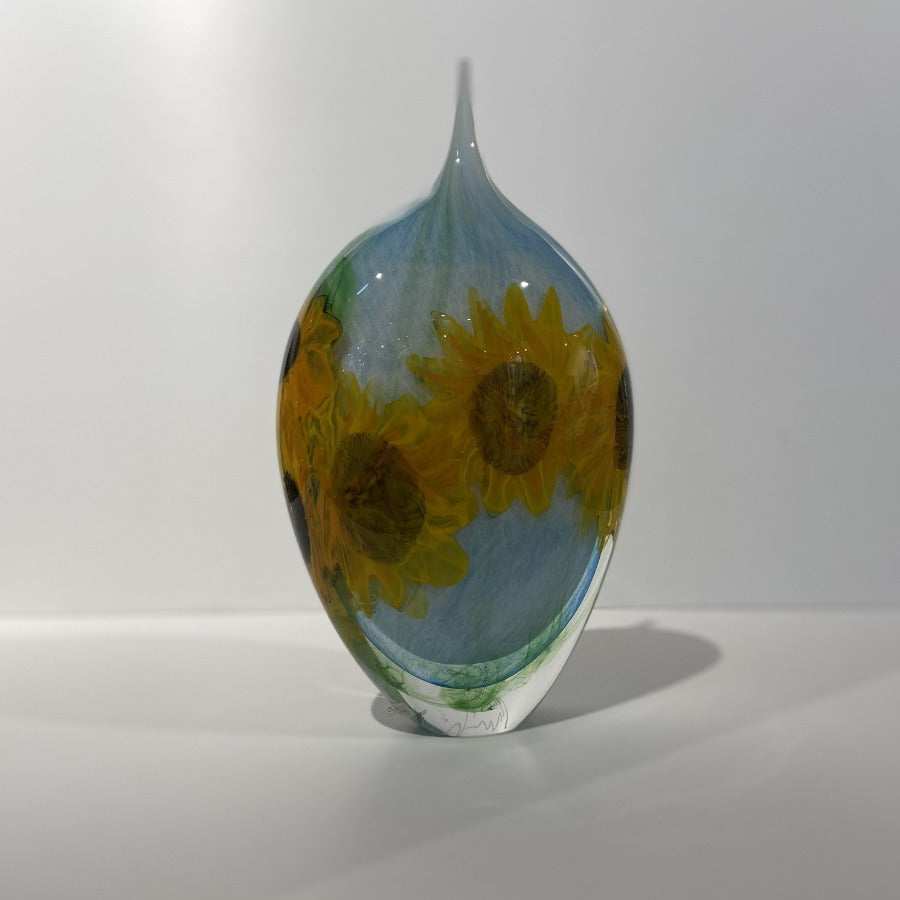 Buy 'Sunflowers' blown glass by Peter Layton online at The Biscuit Factory. Image shows a teardrop shape glass sculpture.  It is light blue with bright yellow sunflower shapes in the glass.