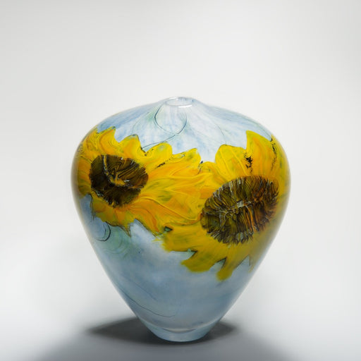 Buy 'Sunflowers' blown glass by Peter Layton online at The Biscuit Factory. Image shows a glass pot which is wide at the top and narrow at the bottom with a small round opening in the centre of the top. It is light blue with two bright yellow sunflower shapes in the glass.