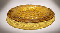 View and buy original glass artwork by Kate Henderson online at The Biscuit Factory. Image shows a mustard coloured plate with a bubbled texture sitting on a white surface and surrounded by a circle of shadow.