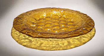 View and buy original glass artwork by Kate Henderson online at The Biscuit Factory. Image shows a mustard coloured plate with a bubbled texture sitting on a white surface and surrounded by a circle of shadow.