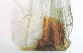 View and buy original glass artwork by Pat Marvell online at The Biscuit Factory. Image shows a section of a glass sculpture resembling crystal, coloured in one section with a rusty orange and pale green. The sculpture sits on a white background.