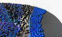 View and buy original glass artwork by Stevie Davies online at The Biscuit Factory. Image shows a section of a black sculpture with metallic blue and purple embellishments from the middle up to the left edge of the image.