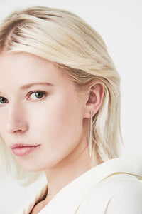 View and buy handmade ethical jewellery by Chloe Solomon at The Biscuit Factory. Image shows a close up photograph of a woman with a long silver earring featuring tubular beads of varying length