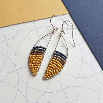 View and buy unique handmade jewellery by Judith Brown online at The Biscuit Factory. Image shows two earrings in a crescent shape with yellow and blue beads.