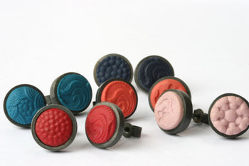 View and buy handmade jewellery by Lindsey Mann online at The Biscuit Factory. Image shows various pairs of polymer clay earrings set in a dark metal, they are dark teal, orange, red, pink and black. The clay is stamped with floral shapes and patterns. 