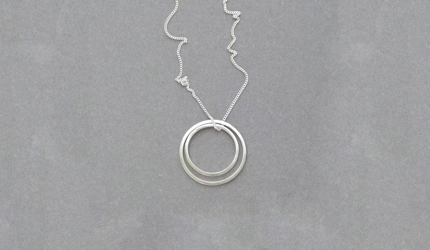 Buy handmade geometric jewellery by Elin Horgan at The Biscuit Factory. Image shows a fine silver chain with a double circle pendant attached sat on a grey background.