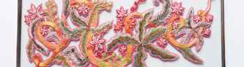 View and buy floral textile wall hangings by Lucy Freeman online at The Biscuit Factory. Image shows a section of framed embroidery on a white background. The embroidery is made up of yellow, orange and pink flowers as well as pastel green leaves.