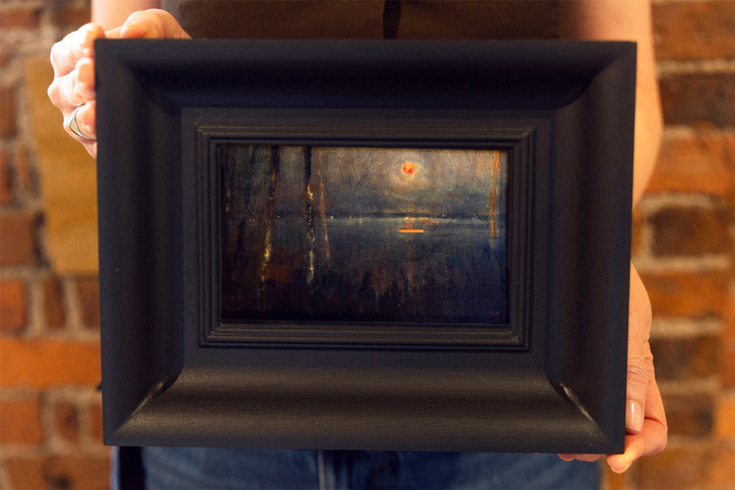Person holding a black-framed painting against a brick wall.