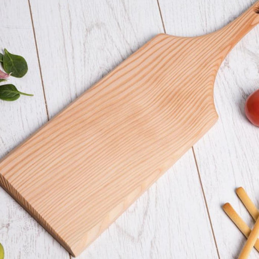 Buy 'Edge Chamfered Serving Board' a handmade wooden serving platter by Majid Lavasani. Image shows a asymmetrically carved light wood serving board with a squared-off each and a long handle. The board sits on a grey wood background with leaves in the top left corner, a the edge of a tomato and breadsticks down the right hand side.