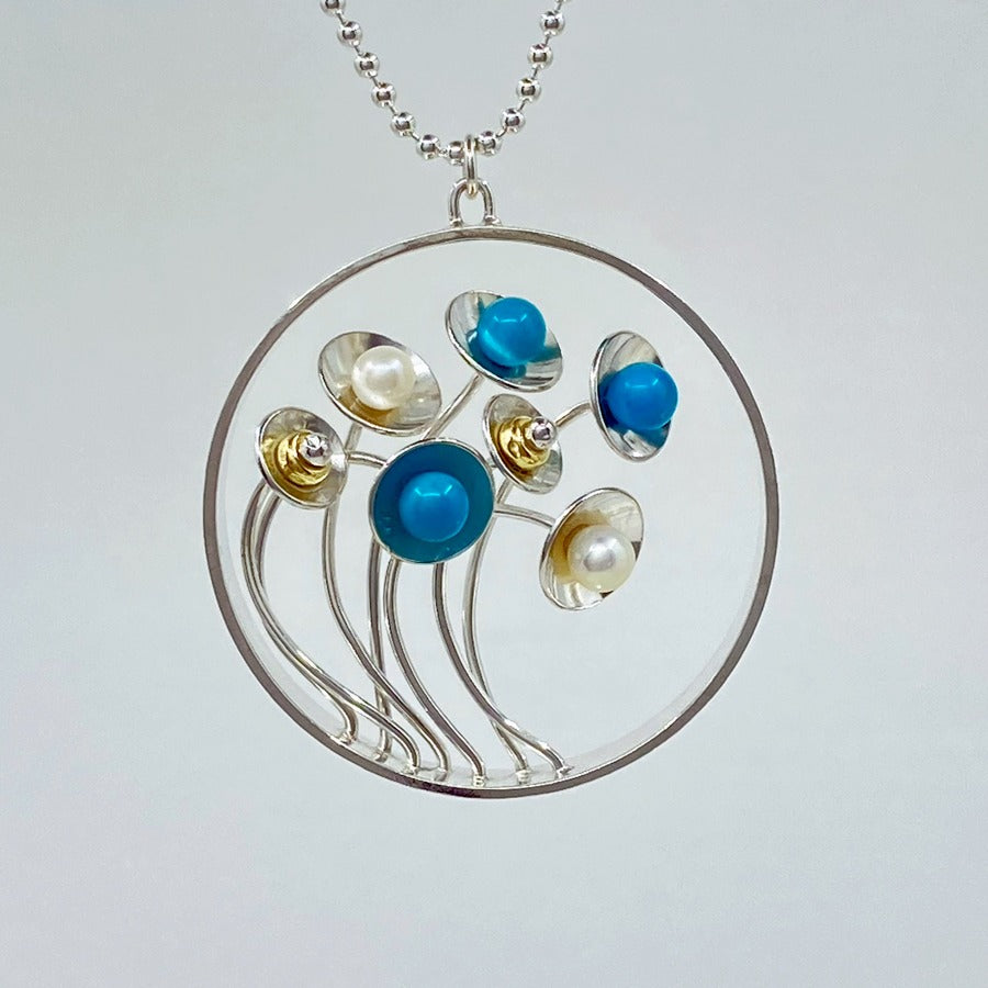'Bouquet' pendant by Yuki Kokai at The Biscuit Factory. Image shows a pendant necklace made of silver wire and discs with white pearl and turquise balls to represent flowers within a silver ring.