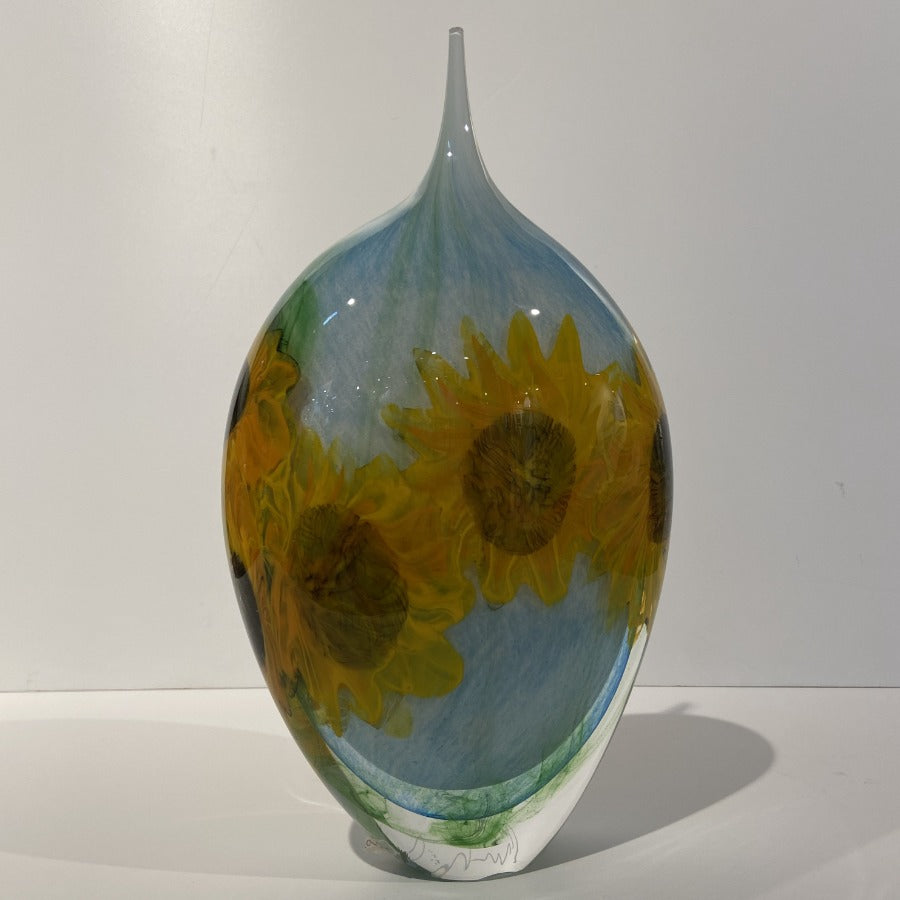 Buy 'Sunflowers' blown glass by Peter Layton online at The Biscuit Factory. Image shows a glass pot which is wide at the top and narrow at the bottom with a small round opening in the centre of the top. It is light blue with two bright yellow sunflower shapes in the glass.