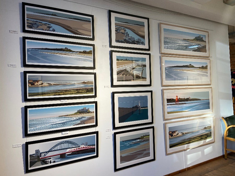 Image shows a selection of framed giclee prints by Ian Mitchell hanging on a white wall at The Biscuit Factory art gallery.