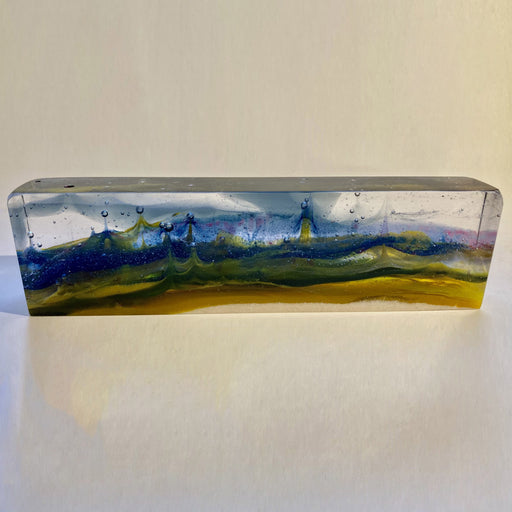 Buy 'In My Dreams' a handmade glass sculpture of a fantasy landscape by Pat Marvell. Image shows a long rectangular block of glass built with clear, blue, green and yellow glass to present an abstract landscape within it. The sculpture sits on a white background.