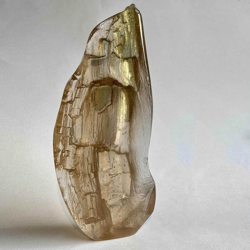 Buy 'Nook' a handmade glass sculpture by Pat Marvell. Image shows a cast glass sculpture with a slight bronze/gold hue in a rough teardrop shape with a bark texture over the surface. The sculpture sits on a grey background.