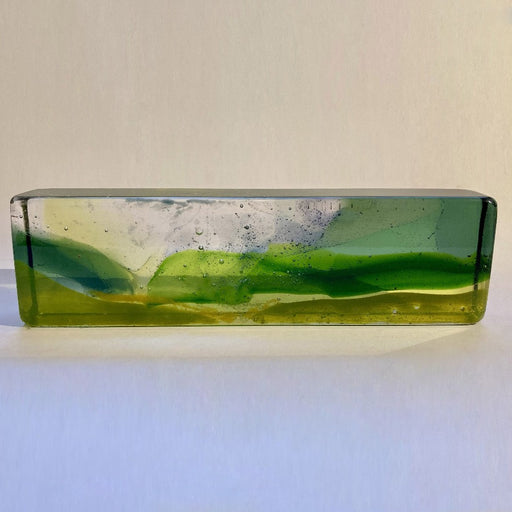 Buy 'Through the Morning Mist' a handmade glass sculpture inspired by the Cornish landscape by Pat Marvell. Image shows a long rectangular glass block built with clear, green and yellow glass to show a vague landscape. The sculpture sits on a white background.