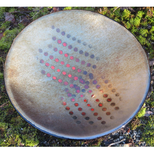 'Shades of 2020 I', a handmade coloured glass dish by Penny Riley-Smith. Image shows a metallic grey circular shallow bowl decorated with dotted patterns in pink, purple and red gradients. The bowl sits on a bed of moss.