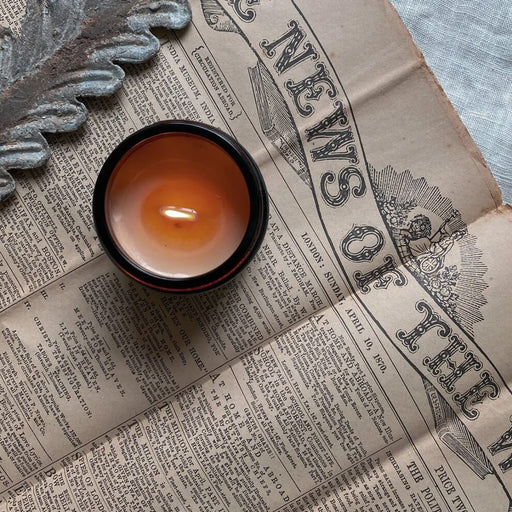 Serene candle by Bous candles, A lit candle in a glass jar on a vintage newspaper. | Handmade gifts for sale at The Biscuit Factory Newcastle.