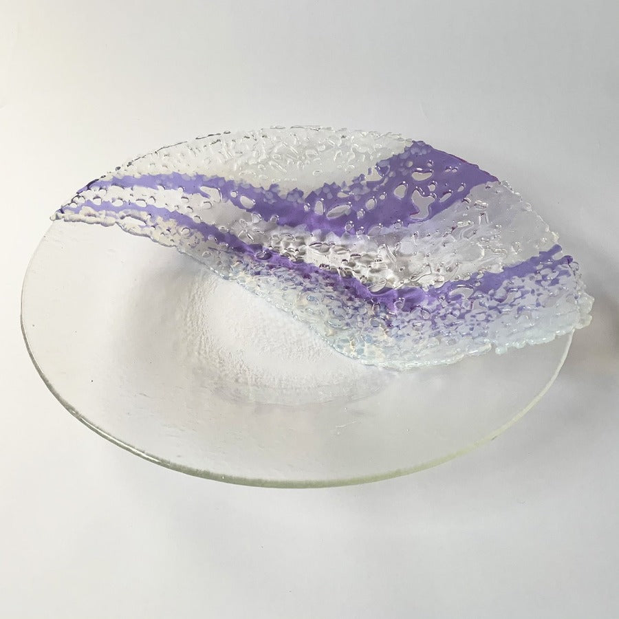 Buy 'Authenticity' a handmade decorative glass dish by Stevie Davies. Image shows a transparent glass dish decorated with fused glass details both transparent and purple in wavy lines across the surface of one half. The dish sits on a white background.