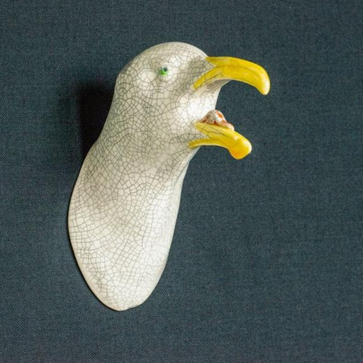 'Buy handmade ceramic sculpture 'Squawking Seagull' by Jackie Summerfield online at the Biscuit Factory. Image shows a ceramic sculpture of a seagull head with a yellow beak, green eyes and crackled glaze, set against a grey backdrop.'