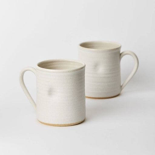 Buy ceramic mug, original handmade craft by Tone von Krogh online at The Biscuit Factory. Image shows a pair of cream ceramic mugs one behind the other. They each have a dimple in the front.